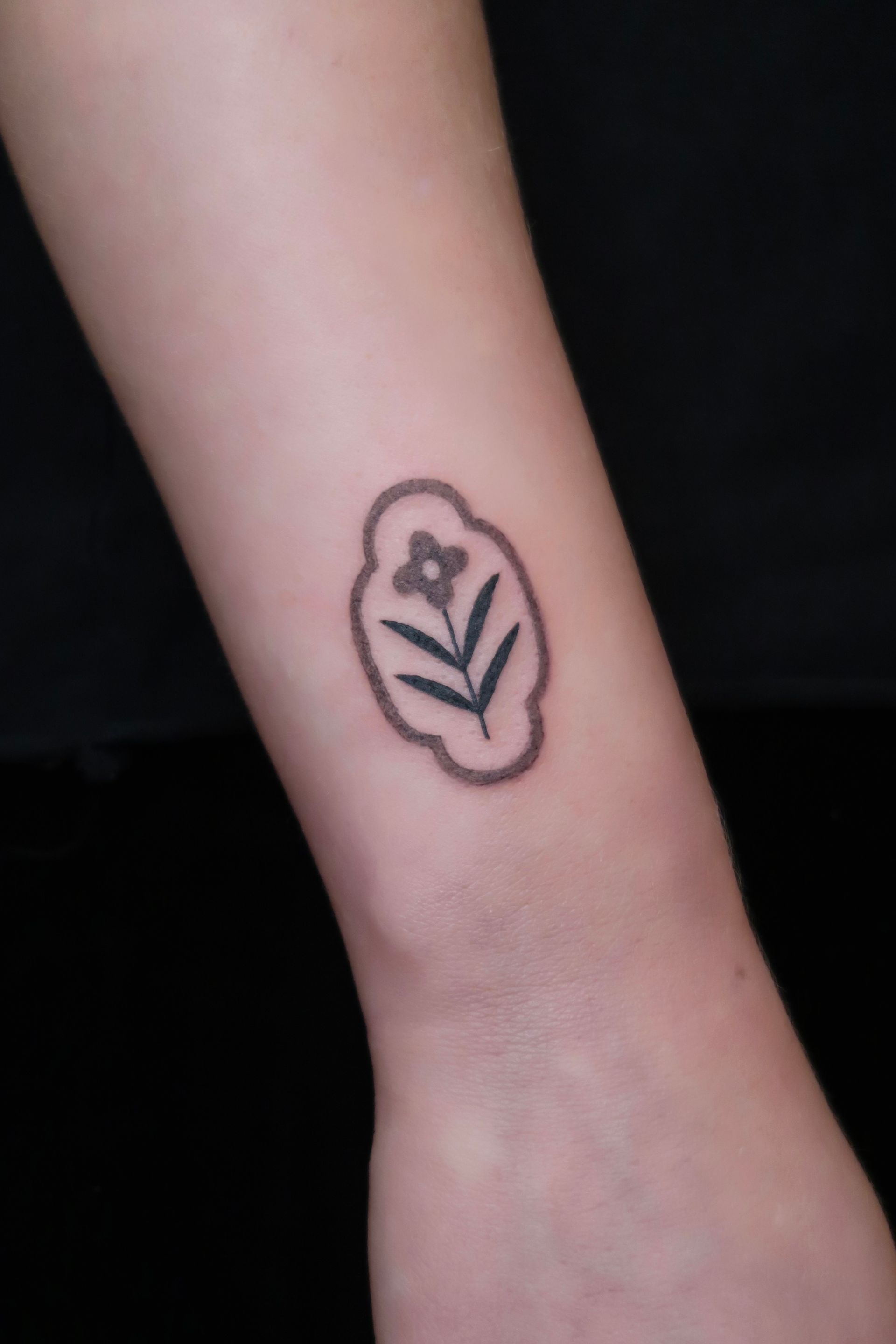 Forearm with a small black flower tattoo outline