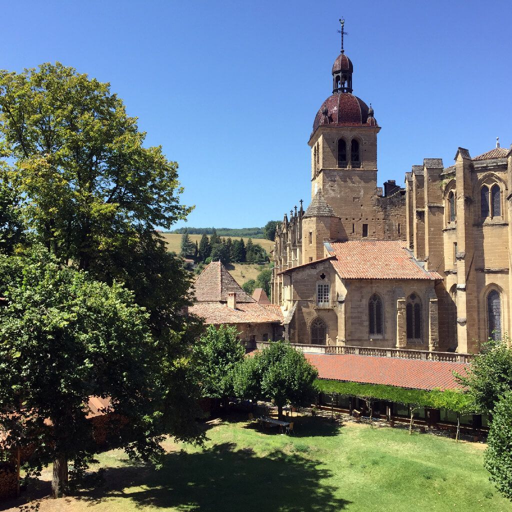 Historic stone church and tower beside a sunlit garden under a clear blue sky