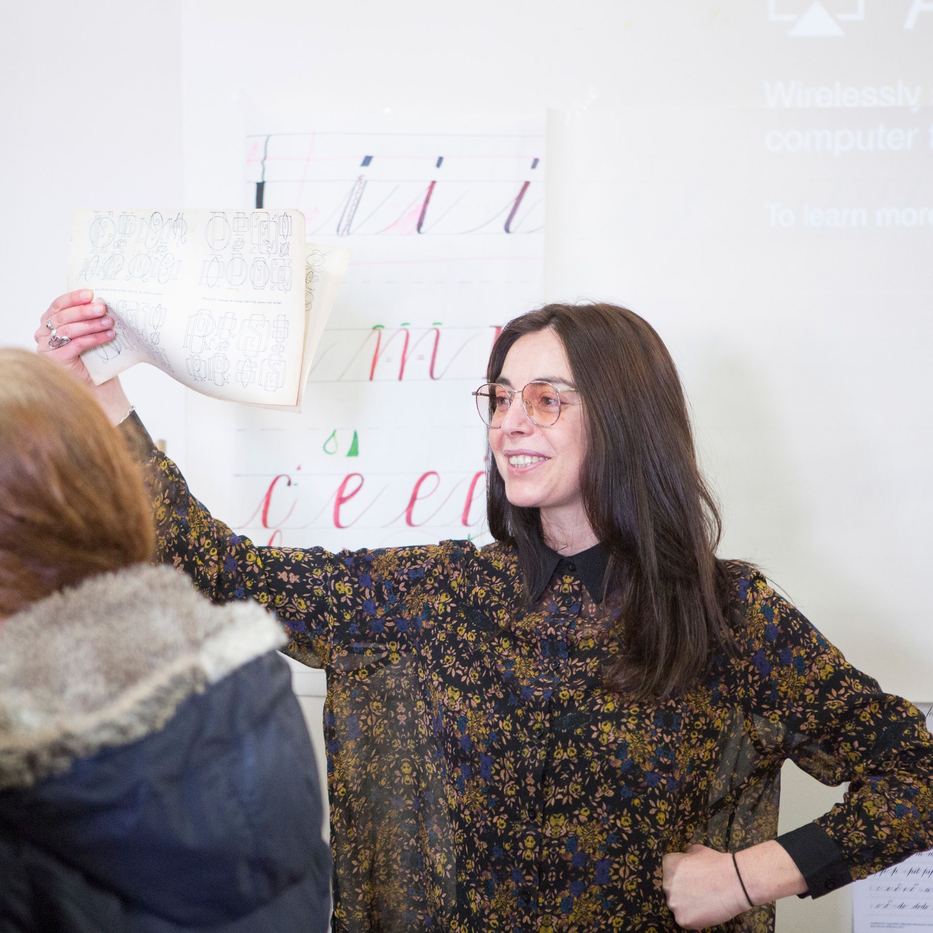 Portrait photo of Maria Montes holding a page while teaching an in-person calligraphy course.