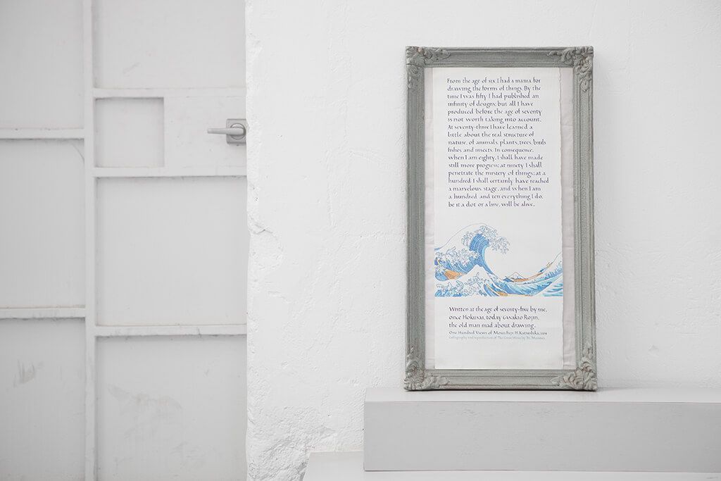 Framed artwork on a white wall above a shelf in a minimalist room