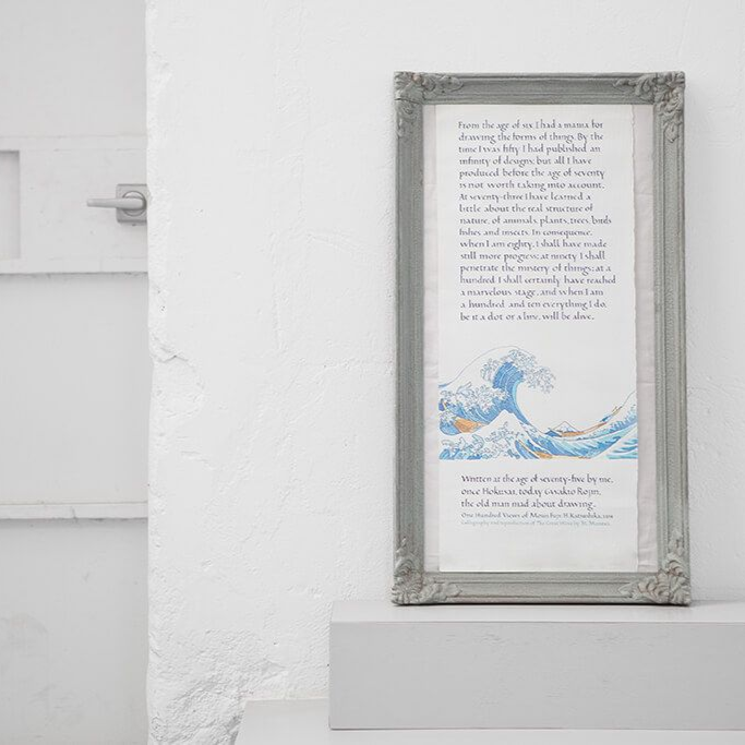 Framed watercolor wave artwork on a white wall above a small shelf