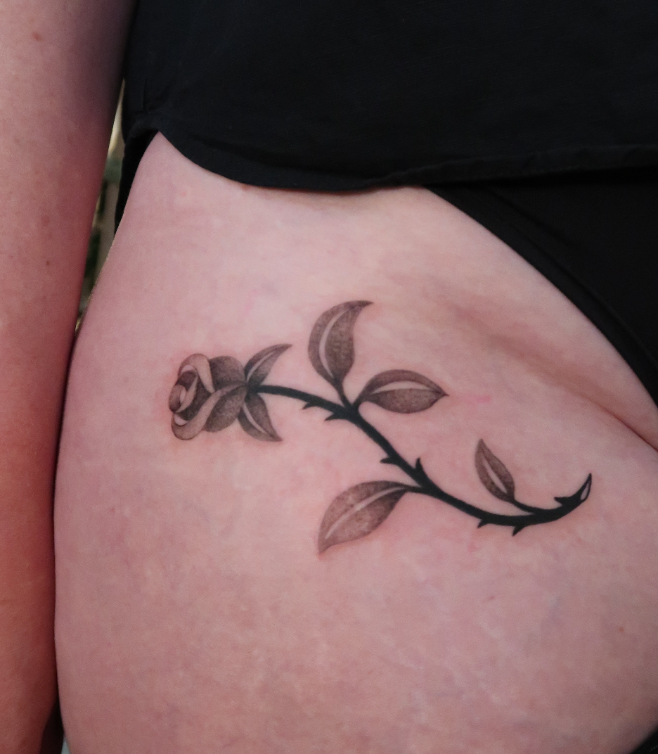 Small black floral tattoo on skin near the waistline.