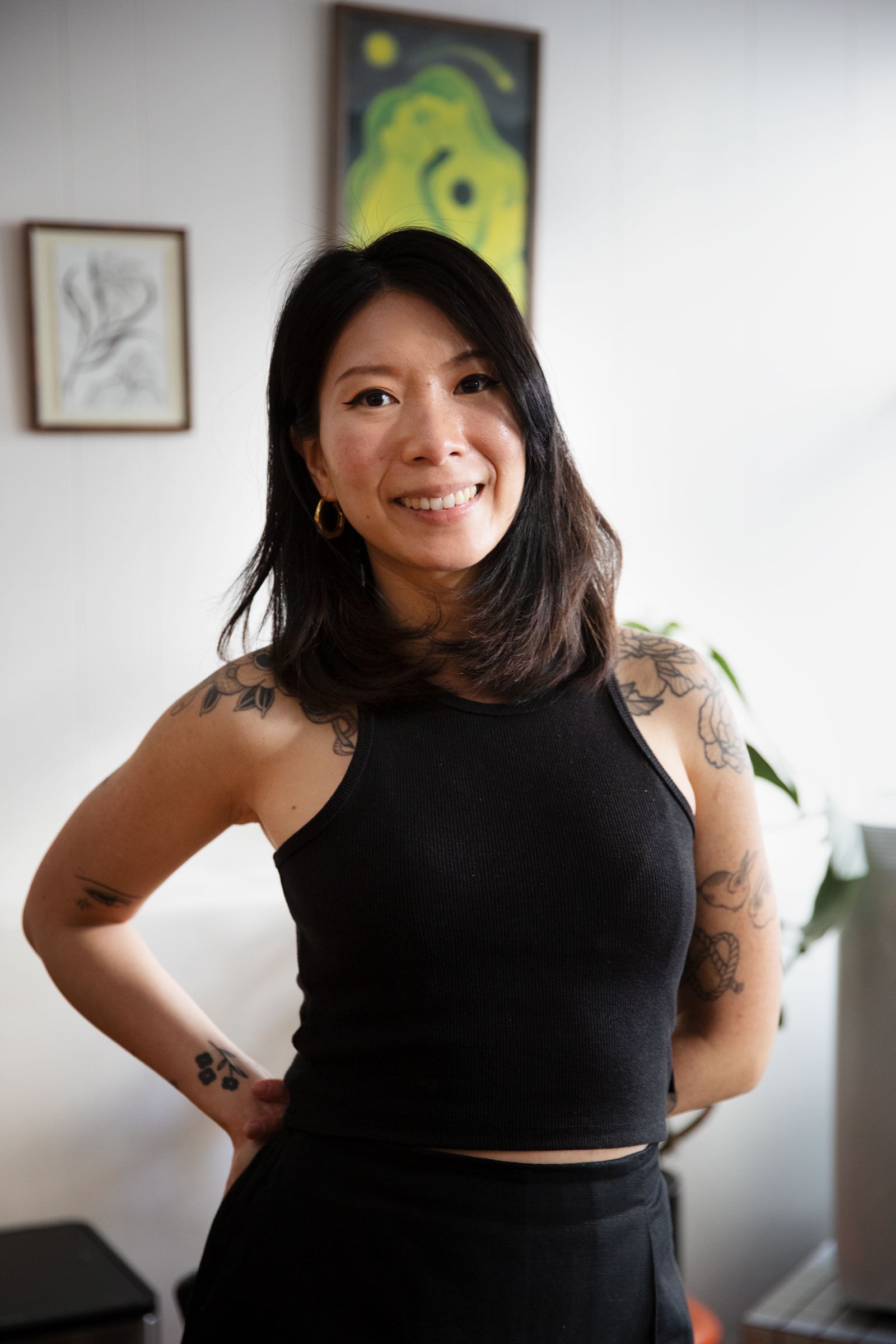 Person standing indoors, smiling with hands on hips, wearing a black sleeveless top.