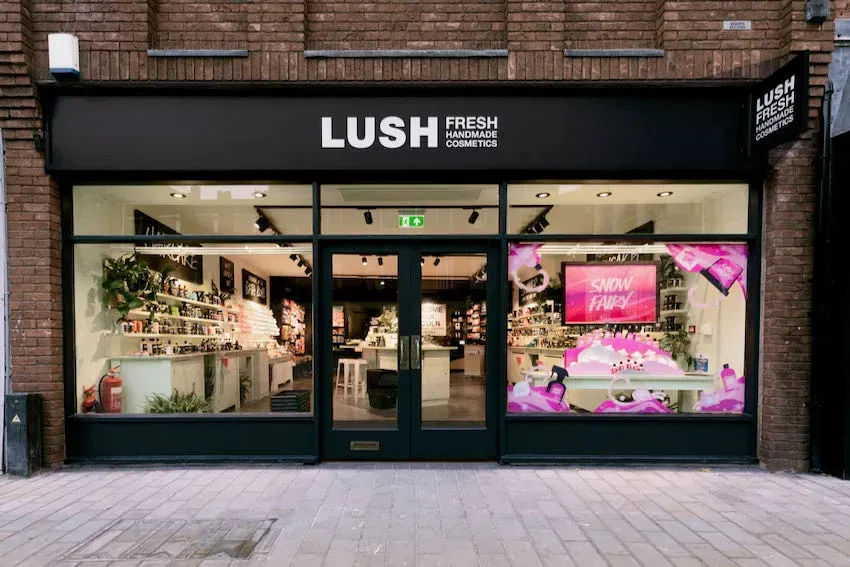 Exterior of Lush cosmetics store with black facade and glass windows. Products displayed inside.