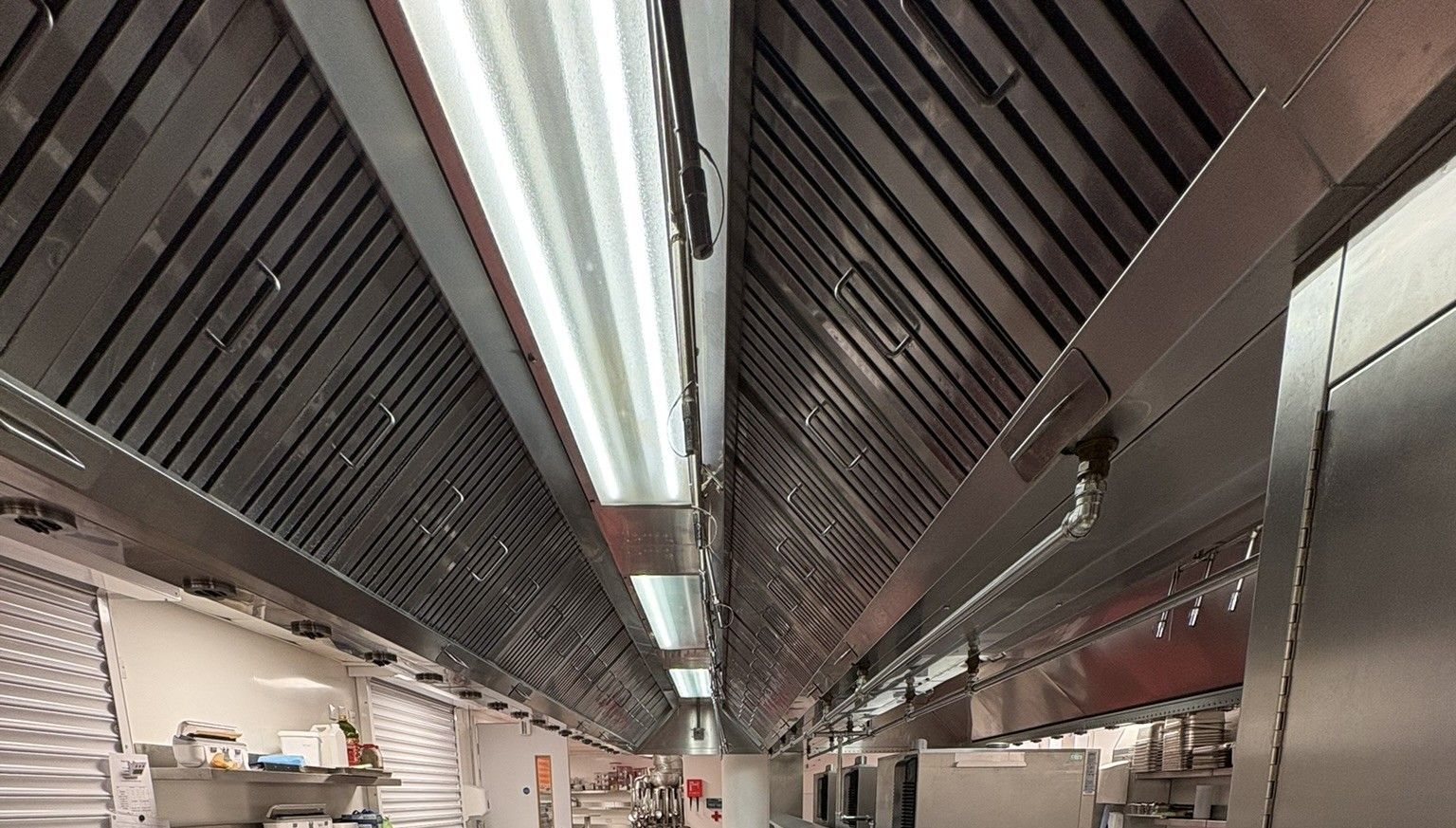 Stainless steel commercial kitchen ventilation hood with overhead lighting.