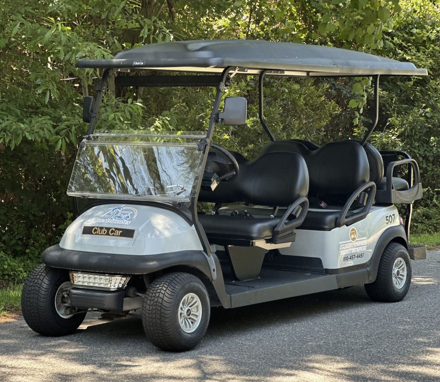 A white golf cart with black seats is parked on the side of the road.