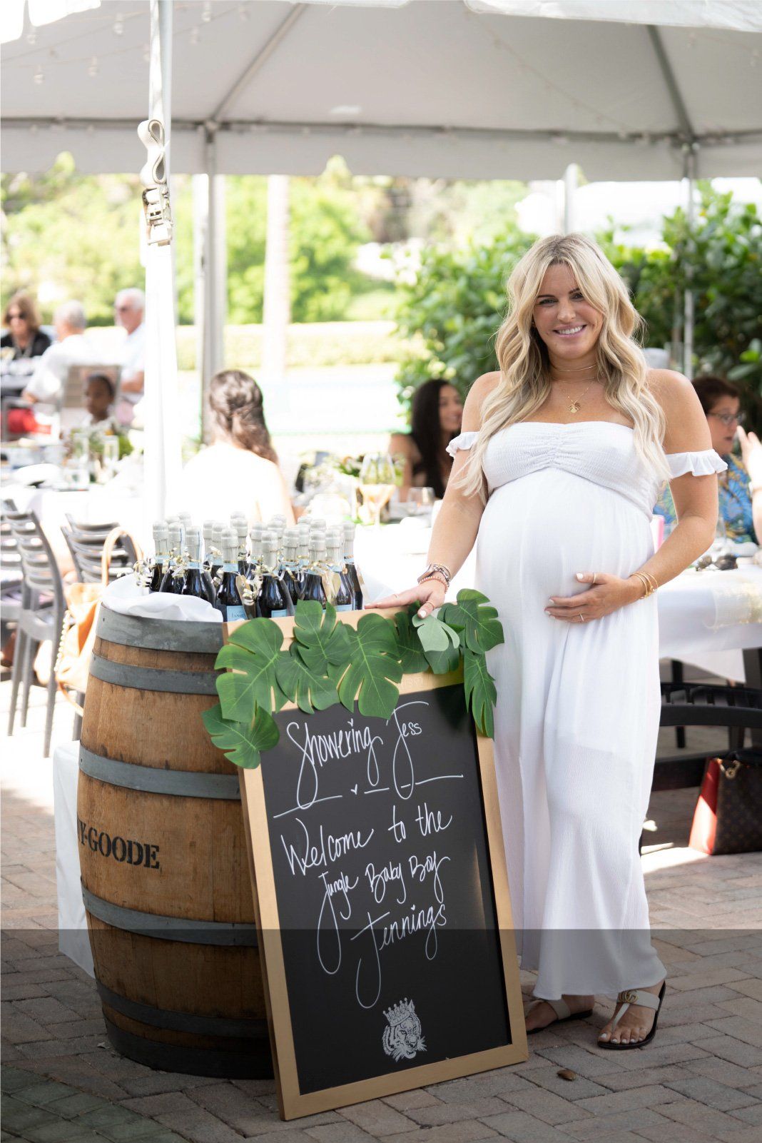 A pregnant woman in a white dress is standing next to a chalkboard.