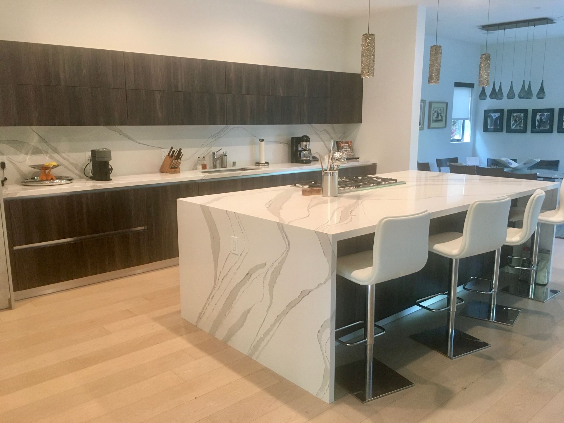 Modern kitchen with dark wood cabinets, marble countertops, large island with seating, and light wood floors.