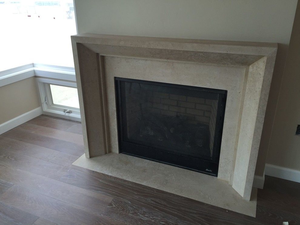 Fireplace with beige stone surround and black firebox, next to a window and wood floor.