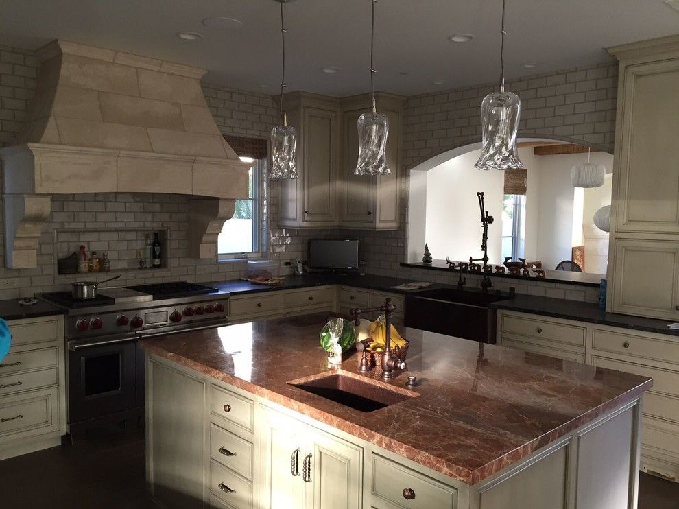 Upscale kitchen with island, reddish countertops, and brickwork backsplash.