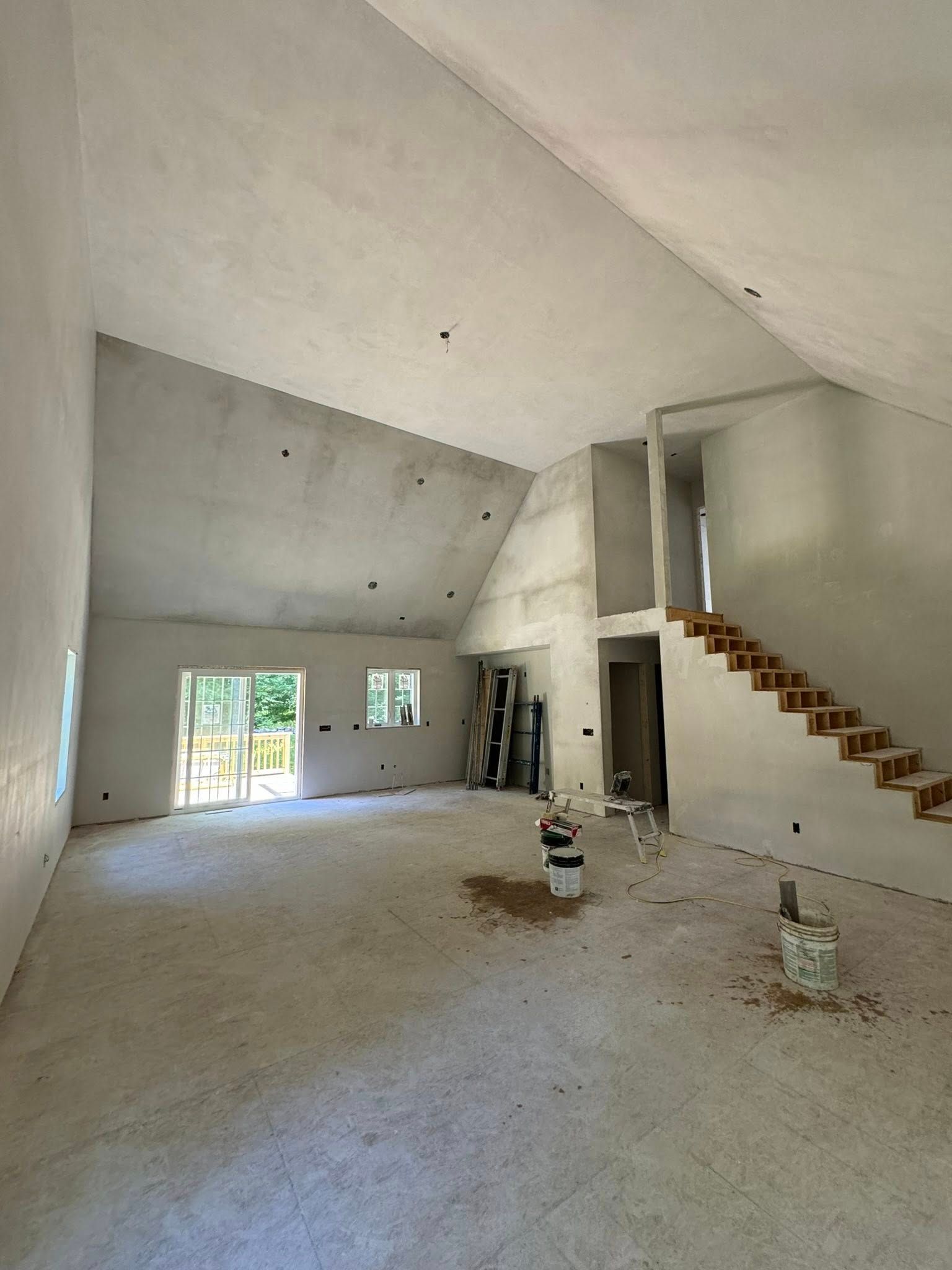 Interior of unfinished house, featuring high ceilings, stairs, and concrete walls.
