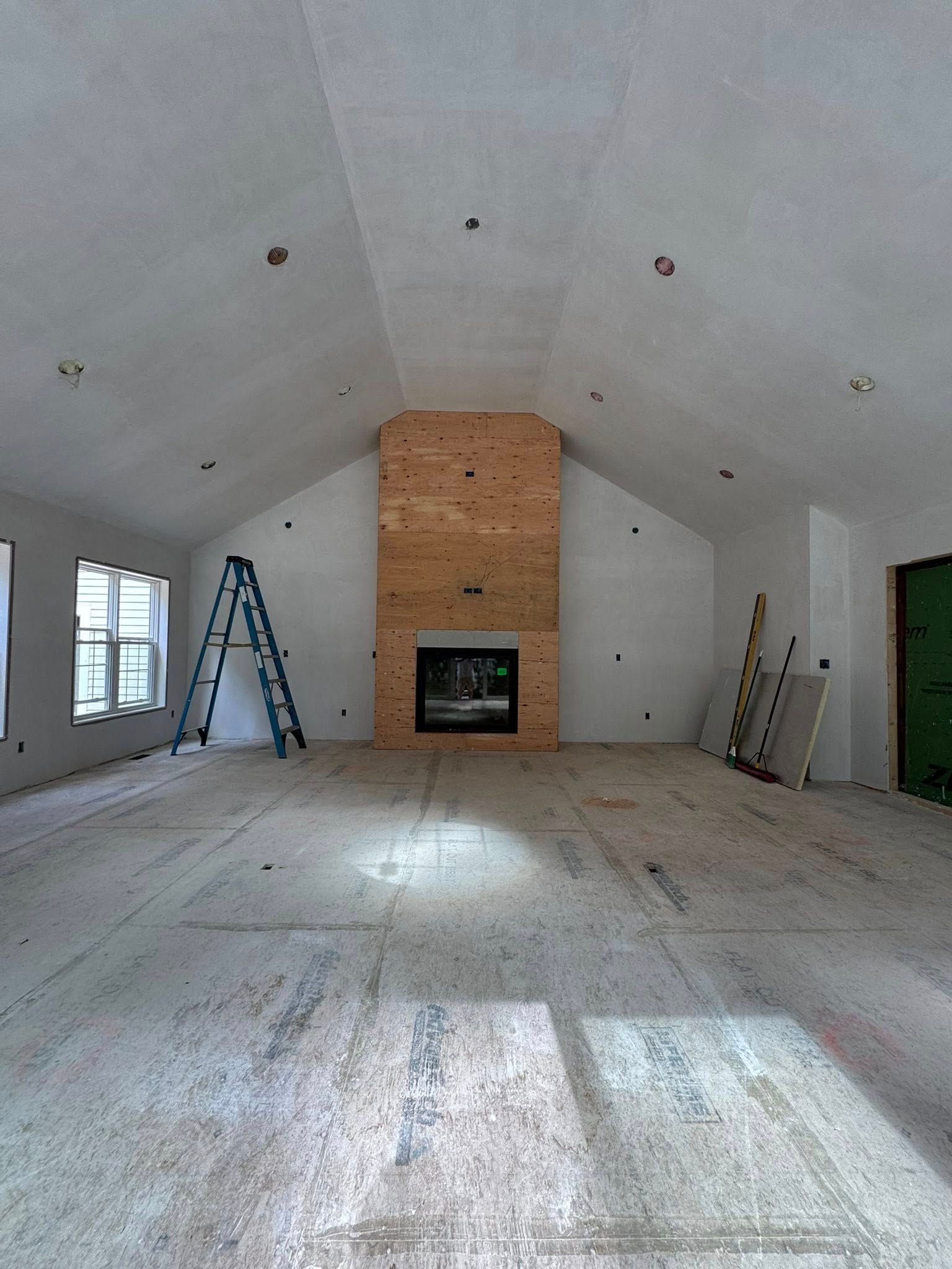 Interior of a room under construction with a fireplace, ladder, and exposed wood and drywall. Interior of a room under construction with a fireplace, ladder, and exposed wood and drywall.