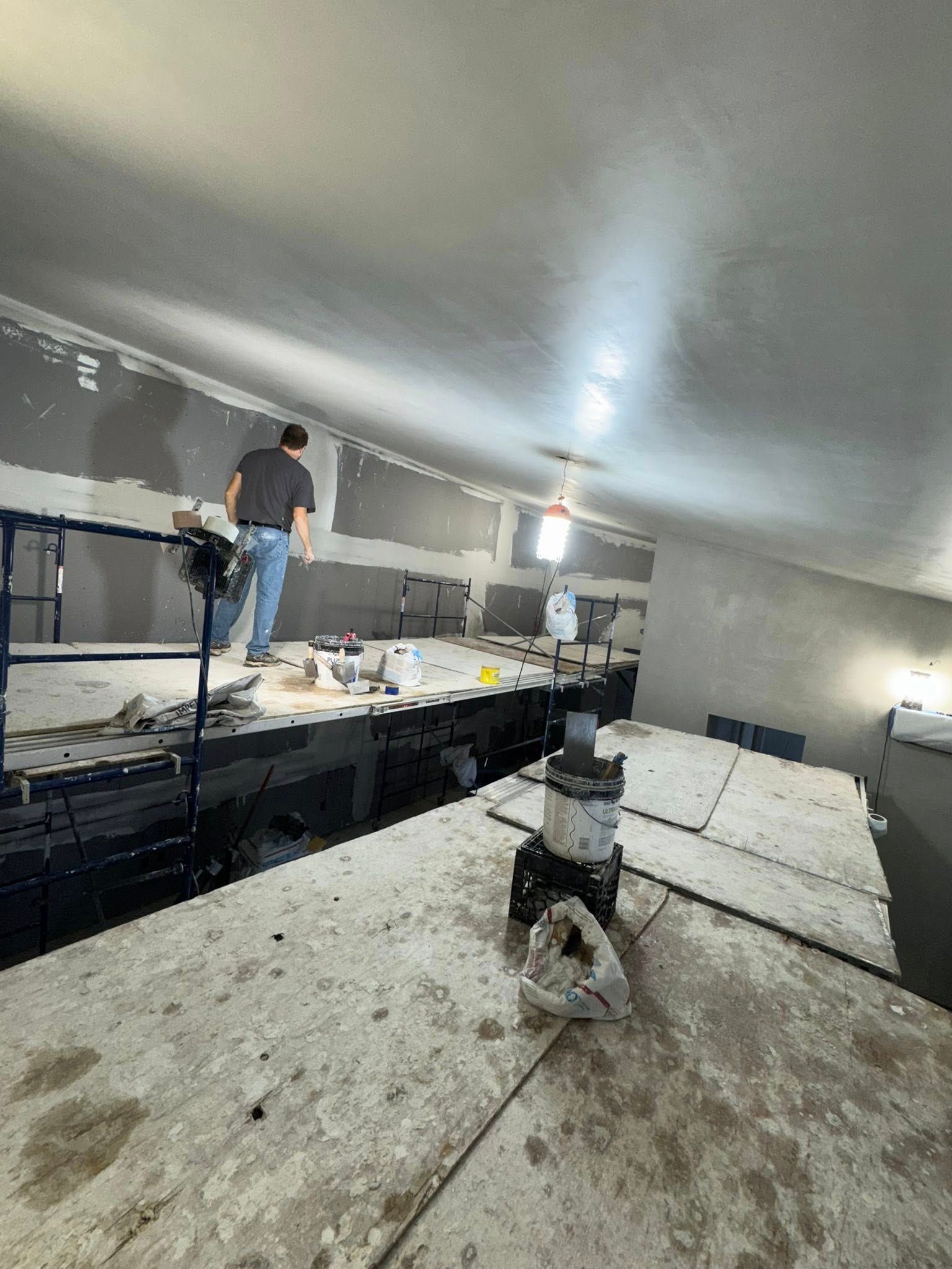 A person on a lift works on drywall in a construction setting.