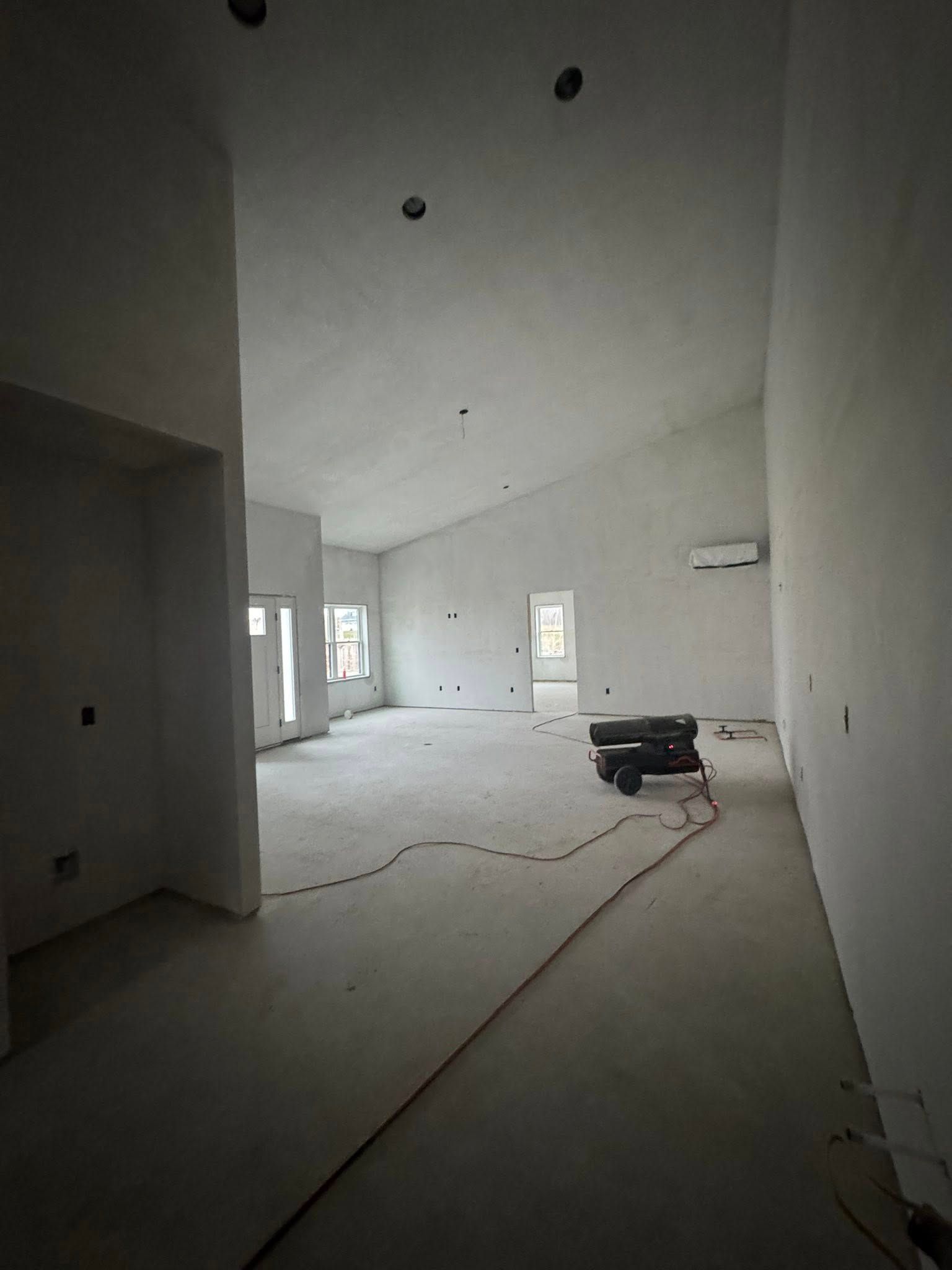 Interior of a room under construction with bare walls, sloped ceiling, and electrical wiring on the floor.