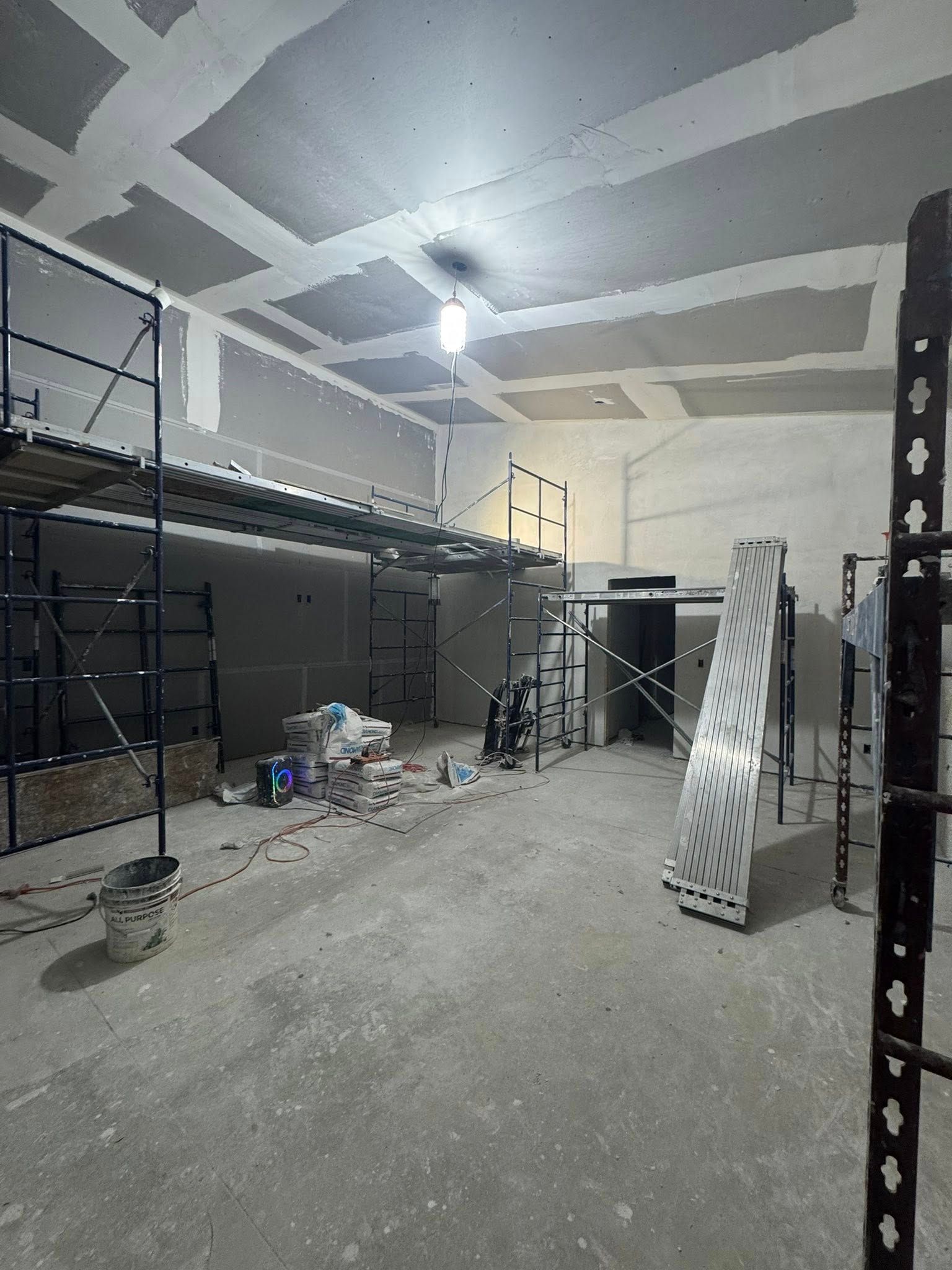 Interior construction site with scaffolding, drywall, and unfinished ceiling.