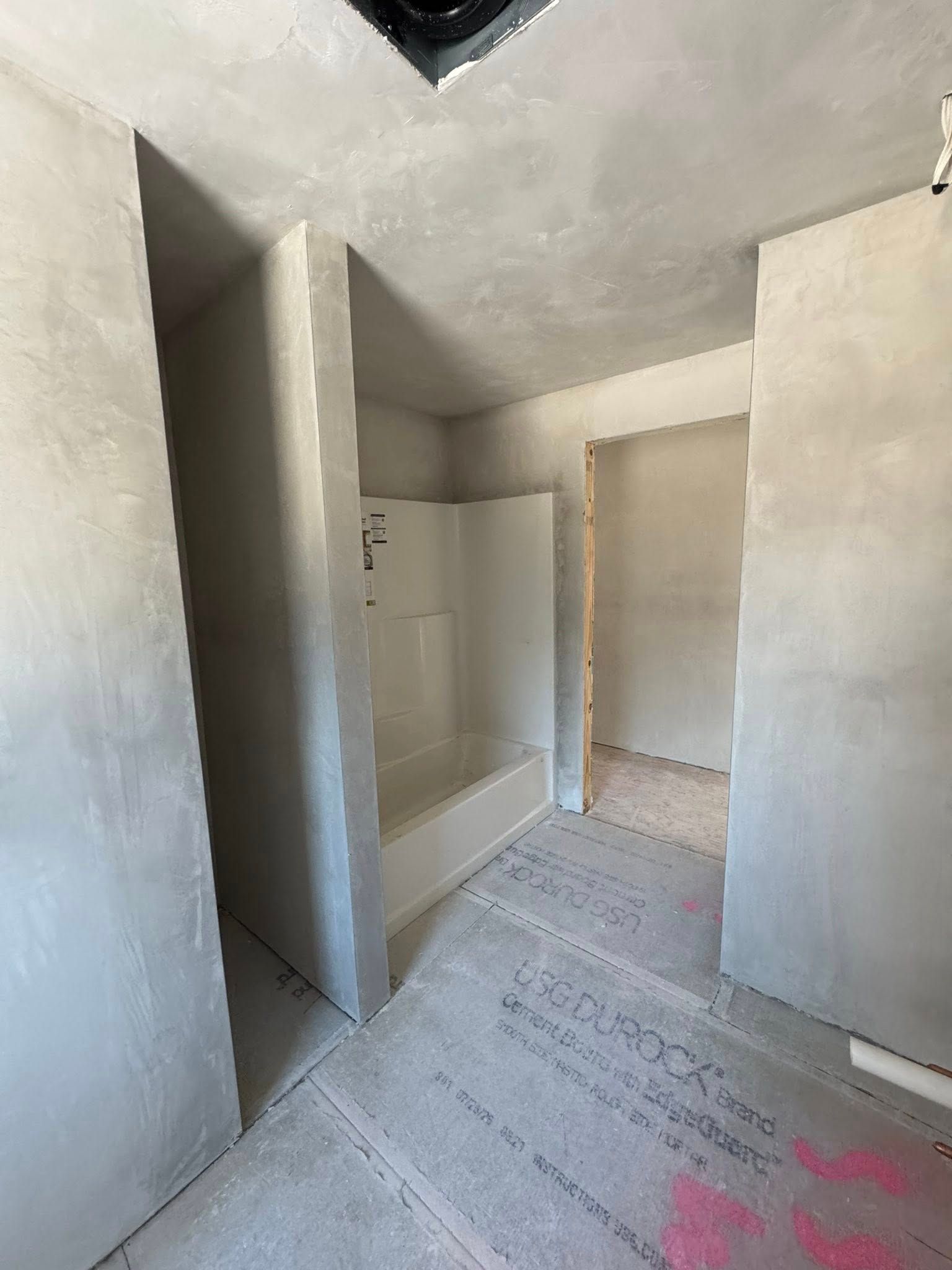 Bathroom under construction, cement walls and floor, shower stall visible.