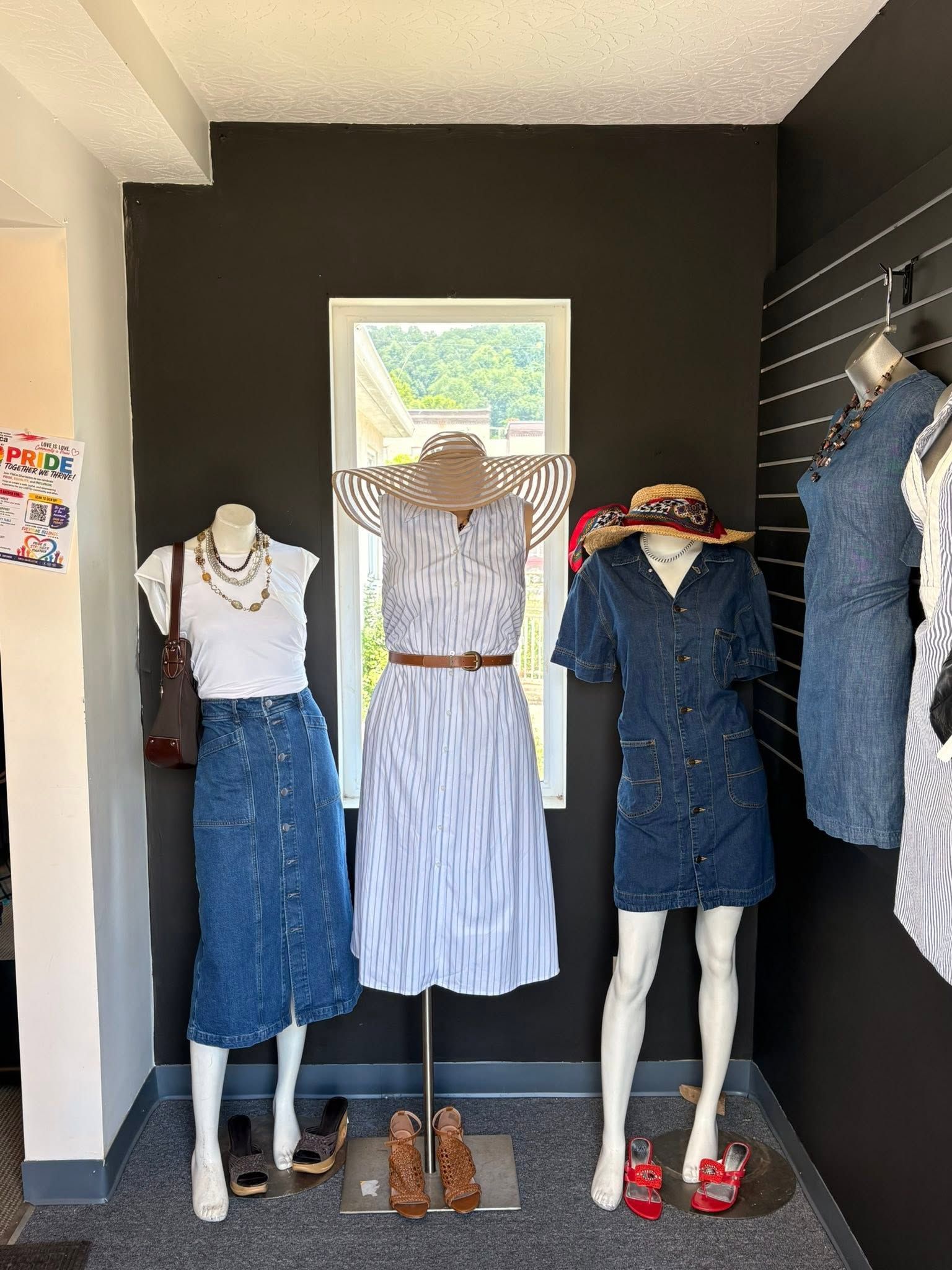 Three mannequins in a shop display wearing blue skirts and dresses against a black wall