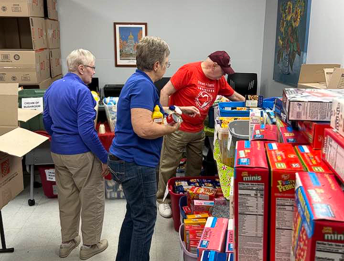 People sorting donated cereal boxes and food items in a room filled with stacked supplies.