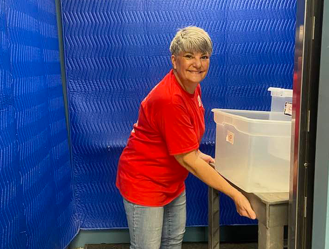 Smiling person in a red shirt loading an item into a clear bin in front of a blue backdrop