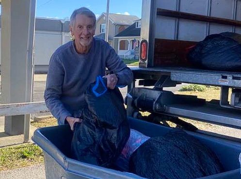 Man loading a black horse into a trailer, standing beside the open trailer ramp outdoors.