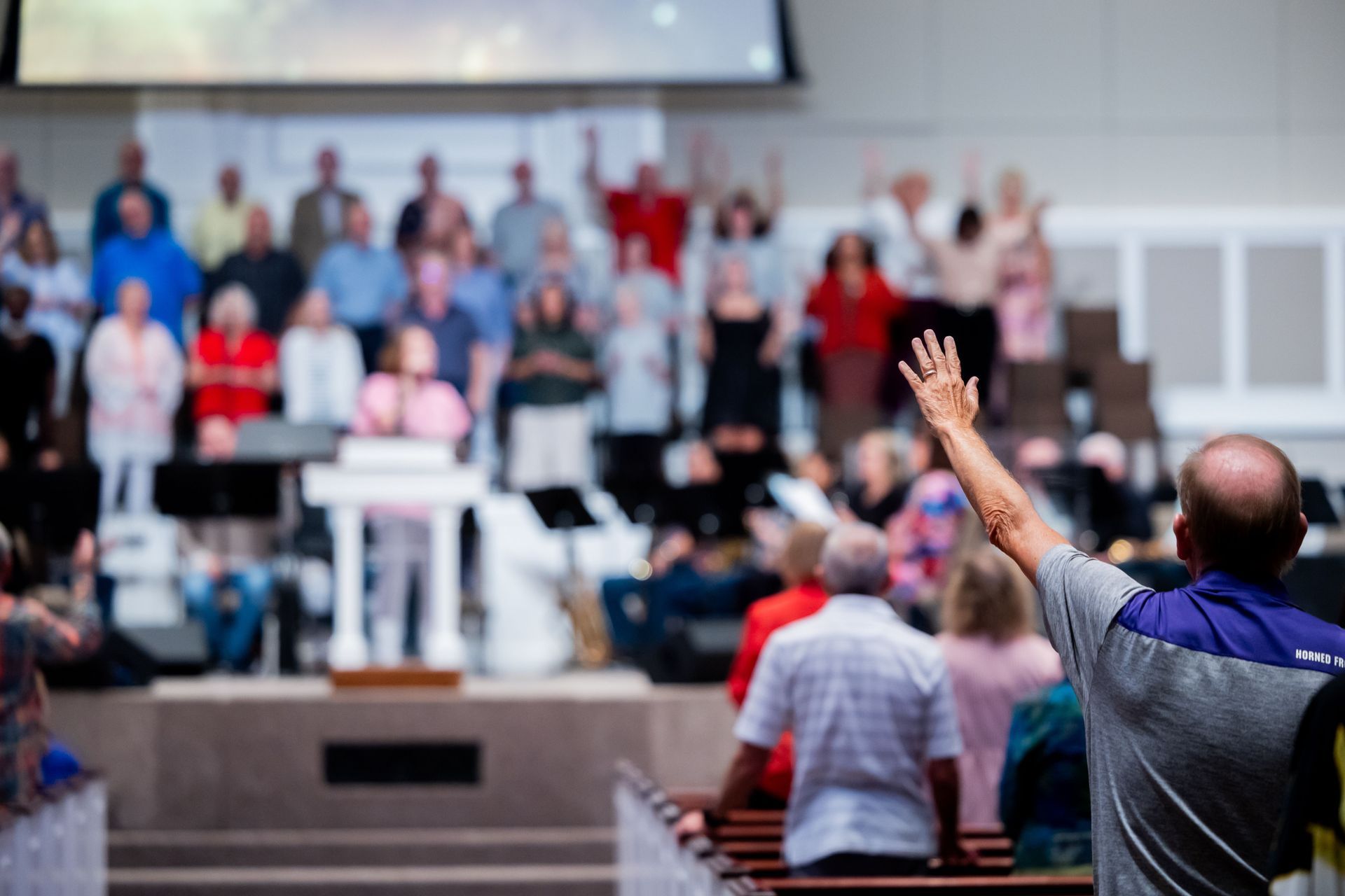 Speaker addressing a standing audience in a church sanctuary, with one person raising a hand.
