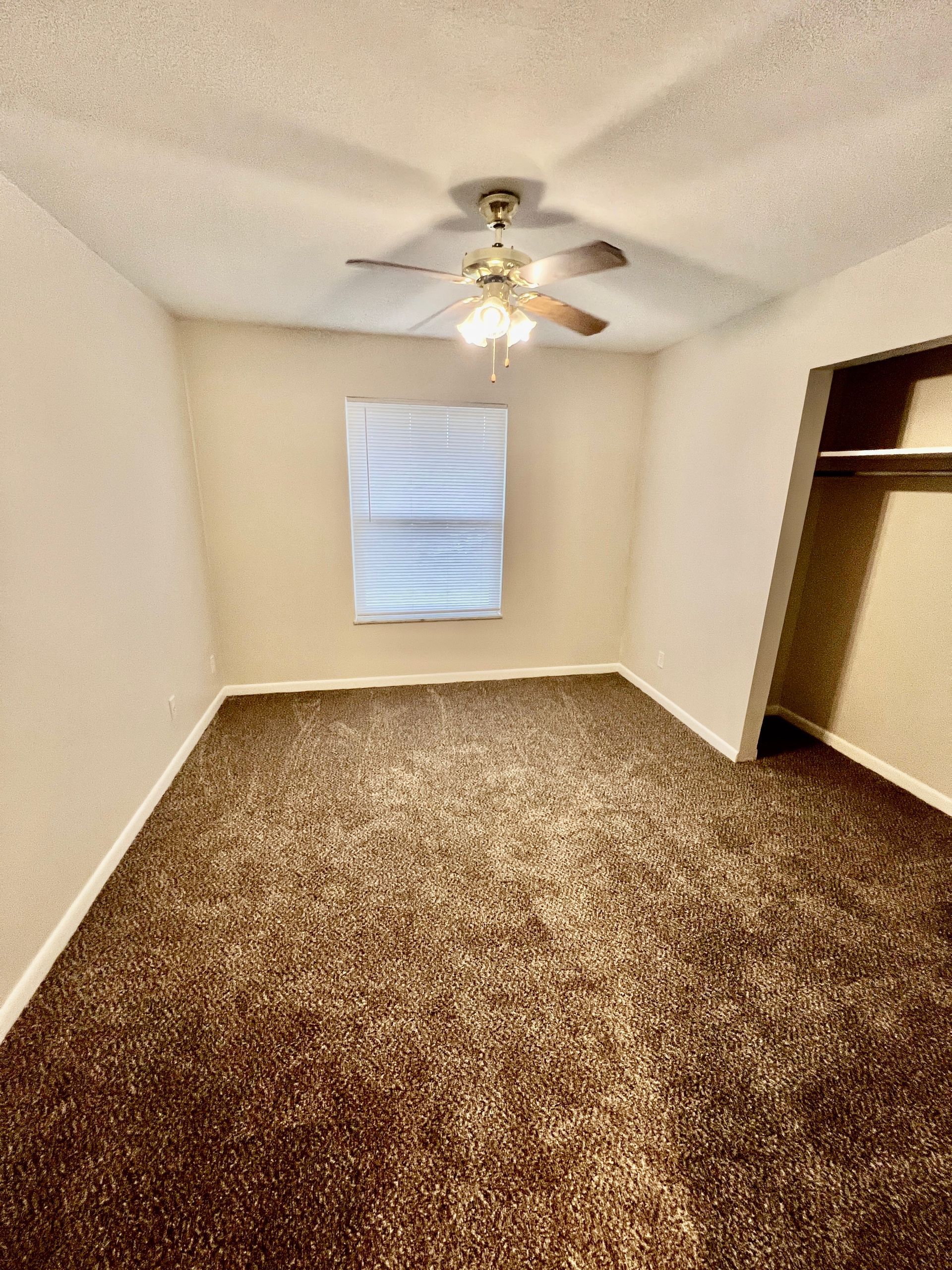 An empty bedroom with a ceiling fan and a window.