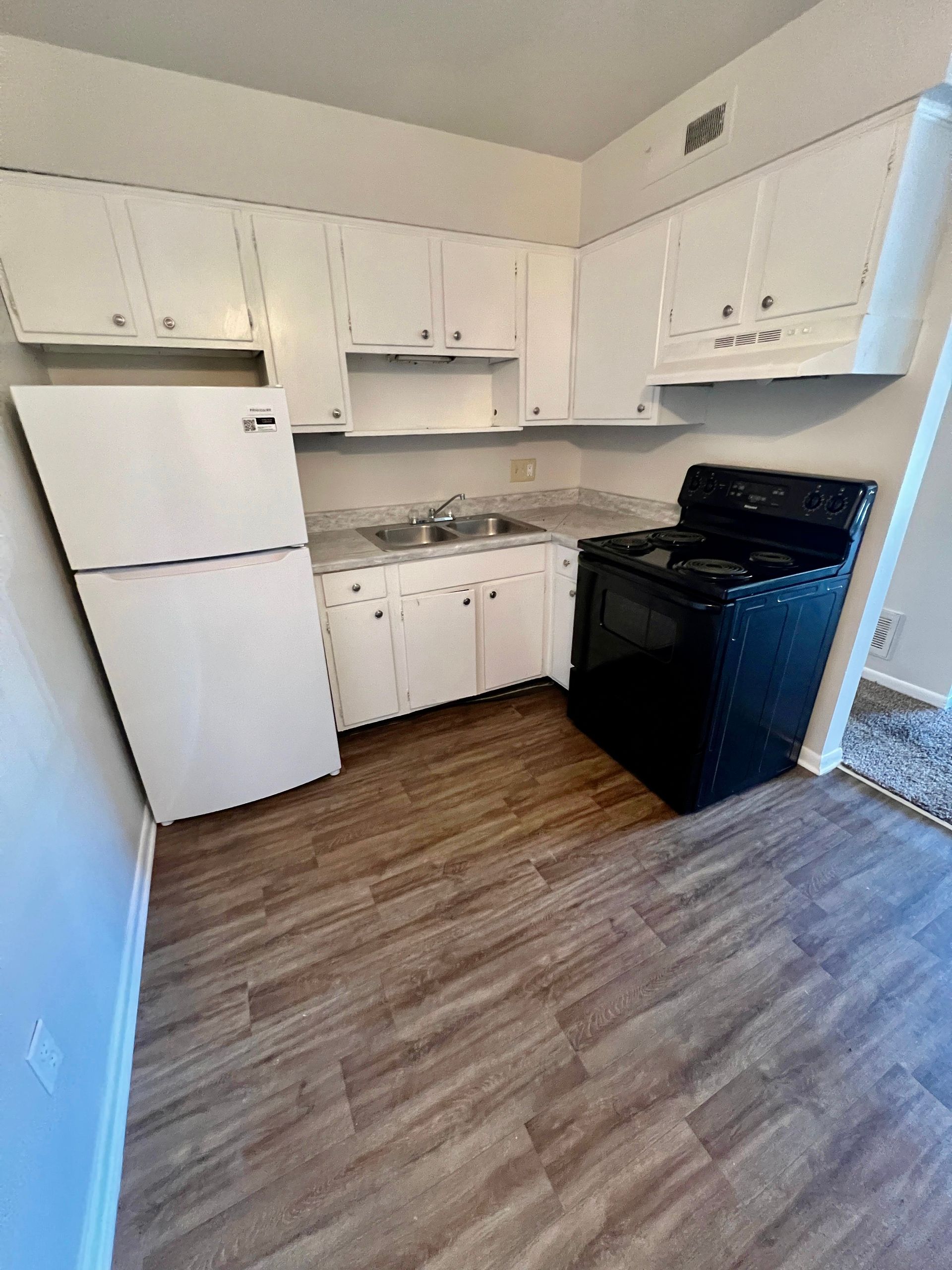 A kitchen with white cabinets , a black stove and a refrigerator.