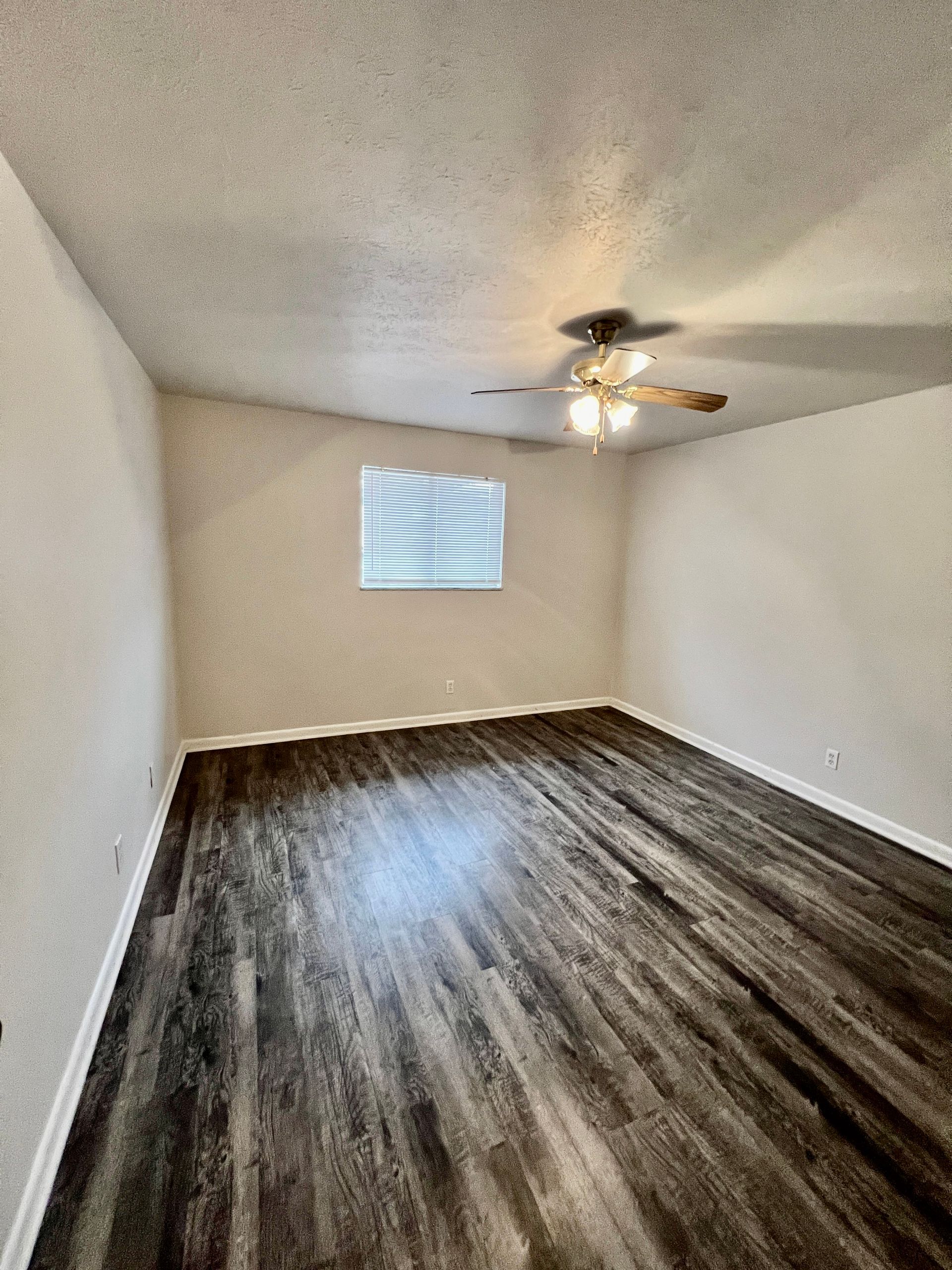 An empty bedroom with hardwood floors and a ceiling fan.