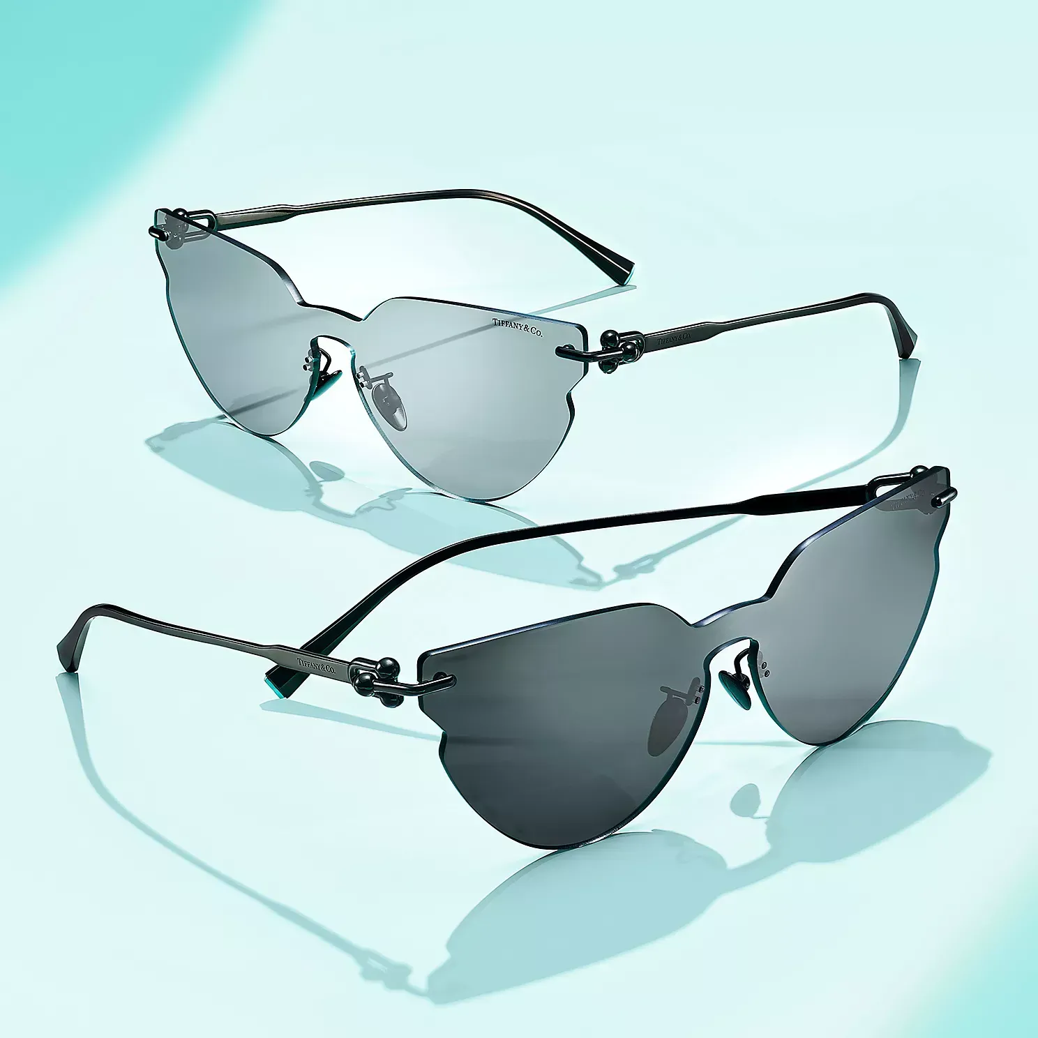 Two pairs of sunglasses are sitting on top of each other on a blue surface.