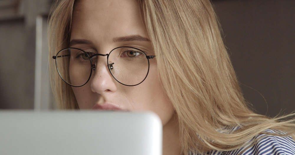A woman wearing glasses is looking at a laptop computer.