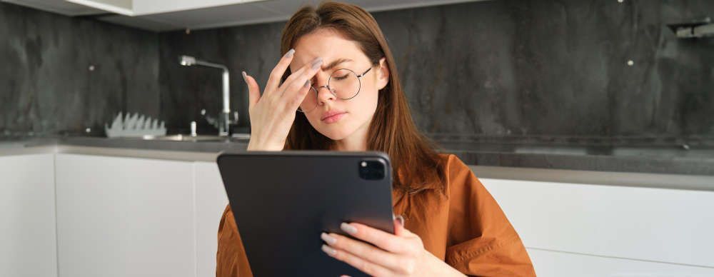 A woman is holding her head while using a tablet computer.