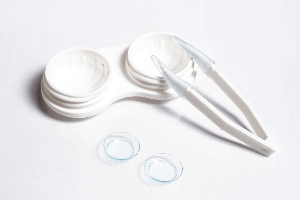 A pair of contact lenses and tweezers on a white surface.