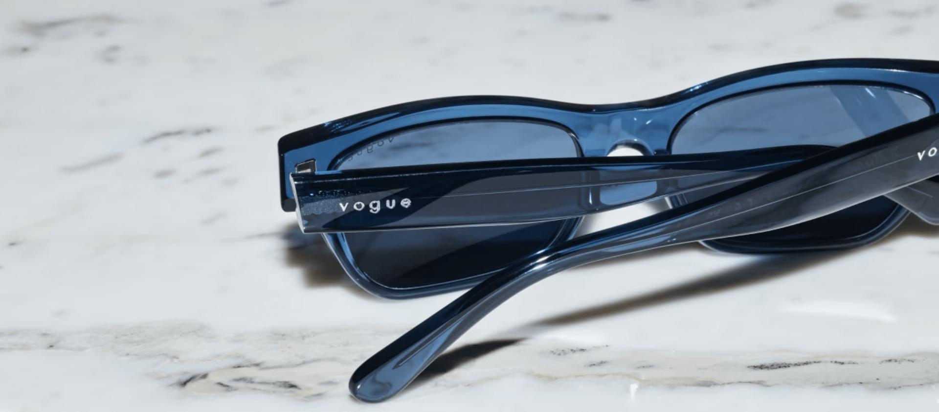 A pair of blue sunglasses are laying on a white surface.