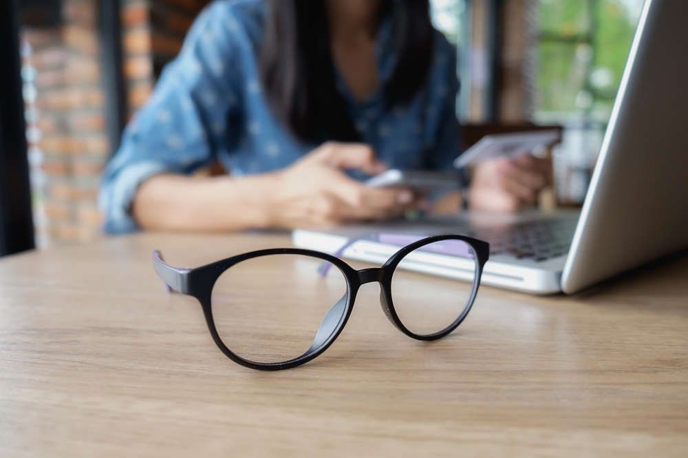 lunettes A pair of glasses is sitting on a wooden table next to a laptop computer.