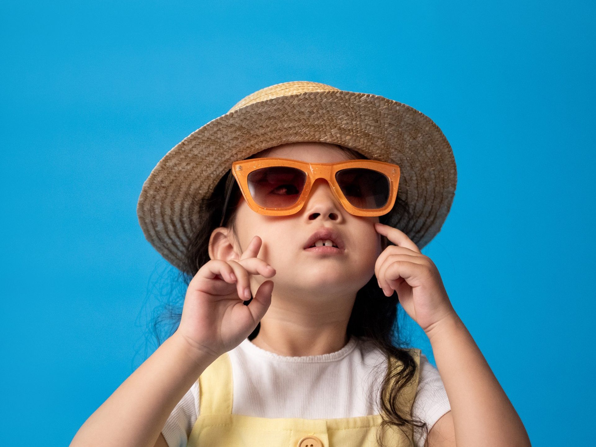A little girl wearing a hat and sunglasses on a blue background.