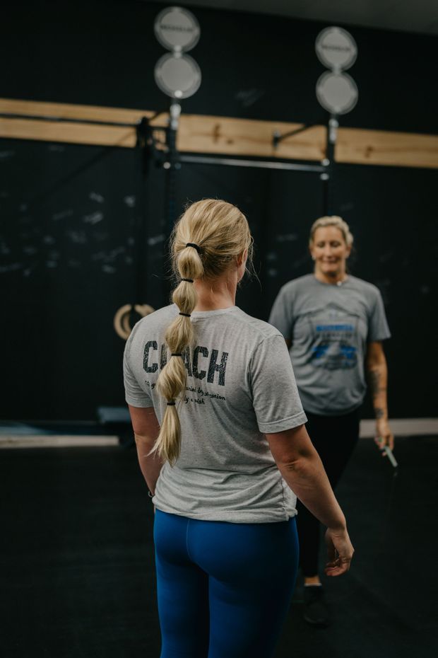 A man is watching a woman do trx exercises in a gym.