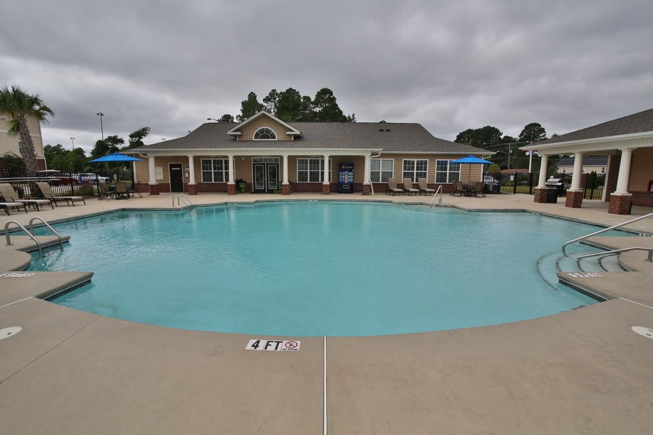 Outdoor community pool with lounge chairs and a clubhouse in the background.