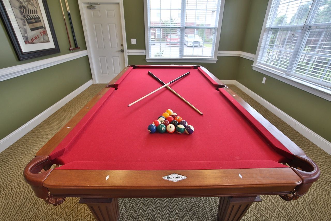 Recreation room with a red pool table, cues, and balls near windows.