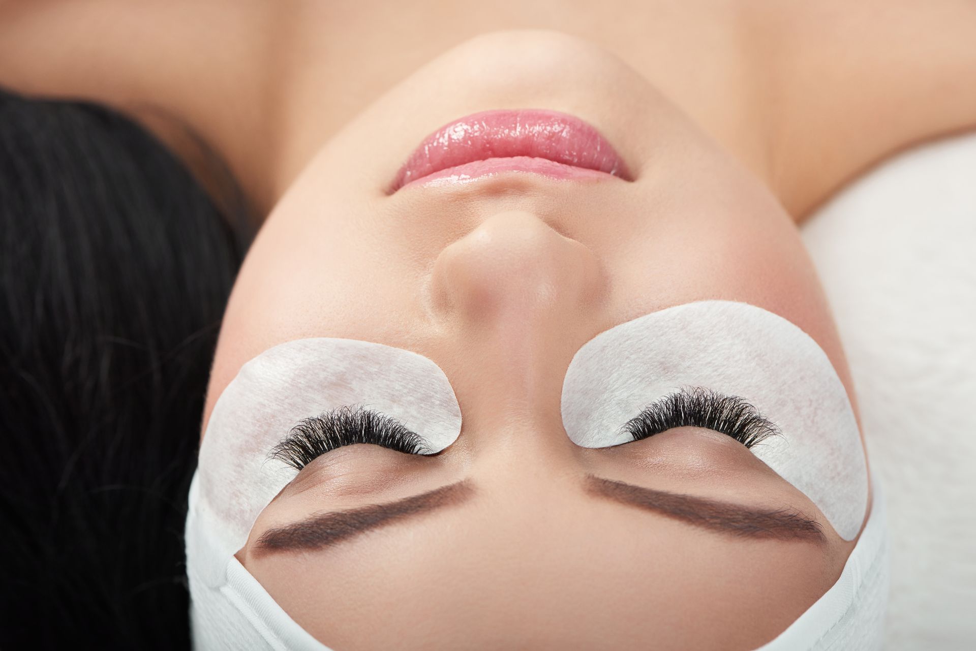 Woman receiving eyelash extensions with under-eye pads during a beauty treatment