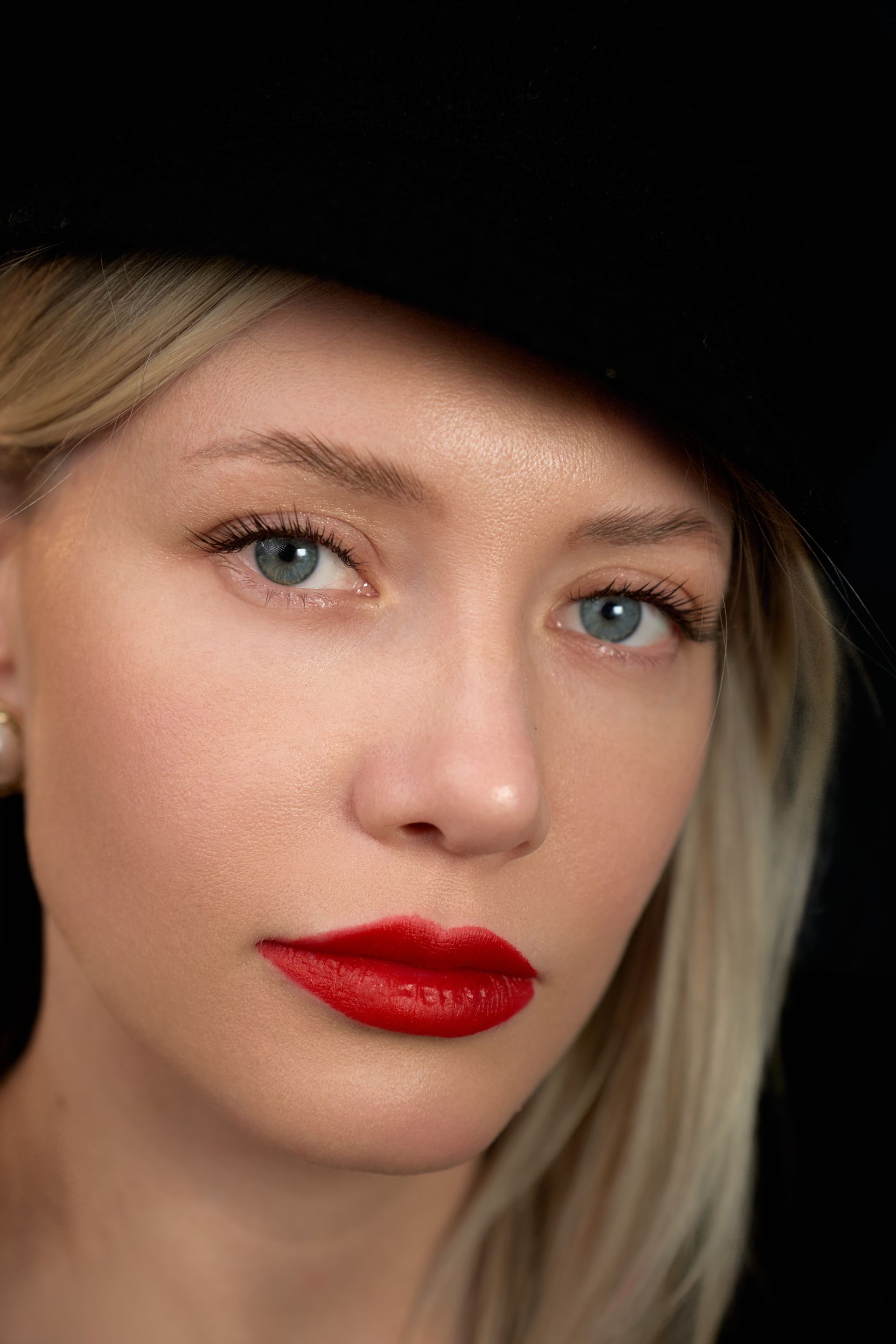 A close up of a woman wearing a hat and red lipstick.