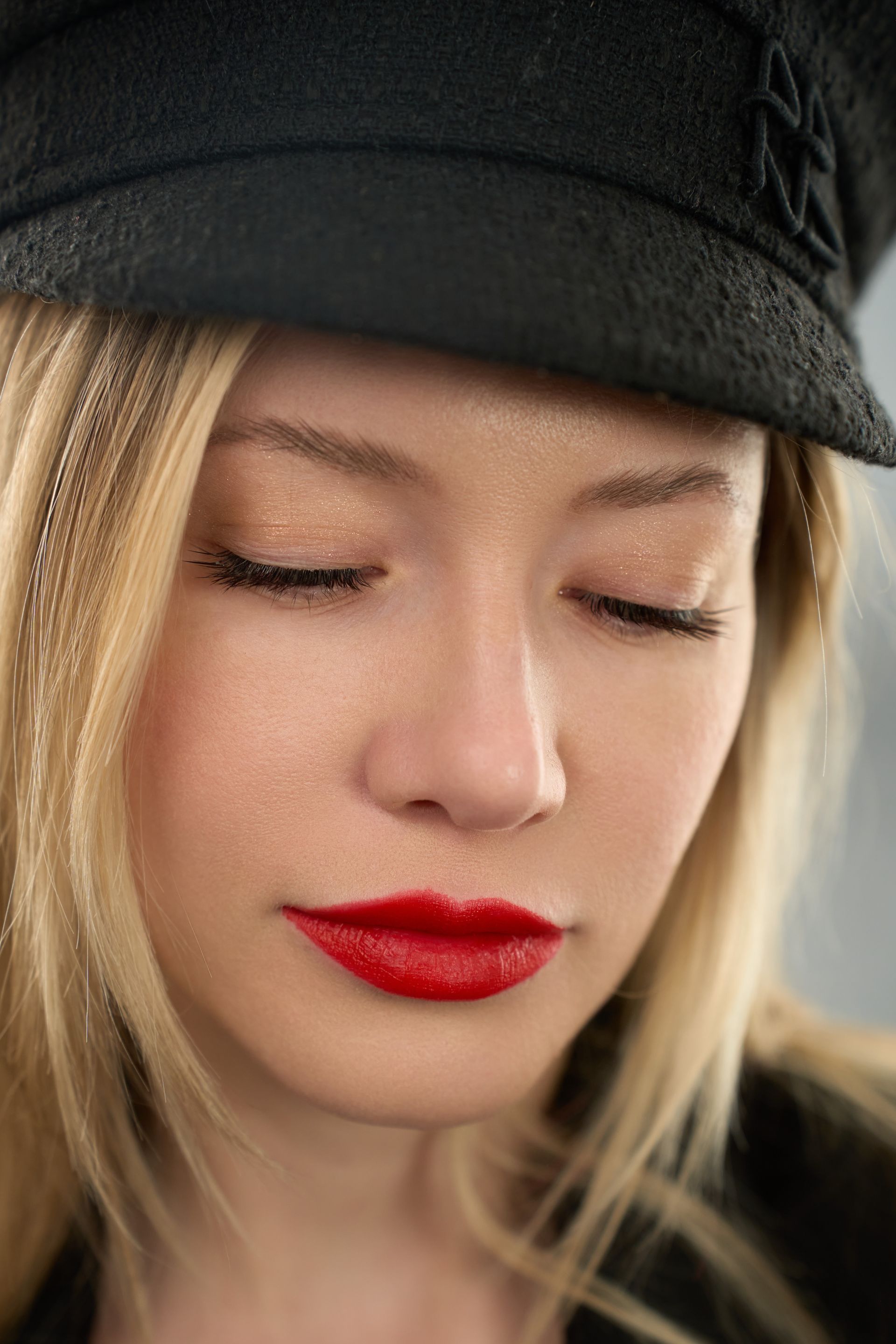 A close up of a woman wearing a hat and red lipstick.