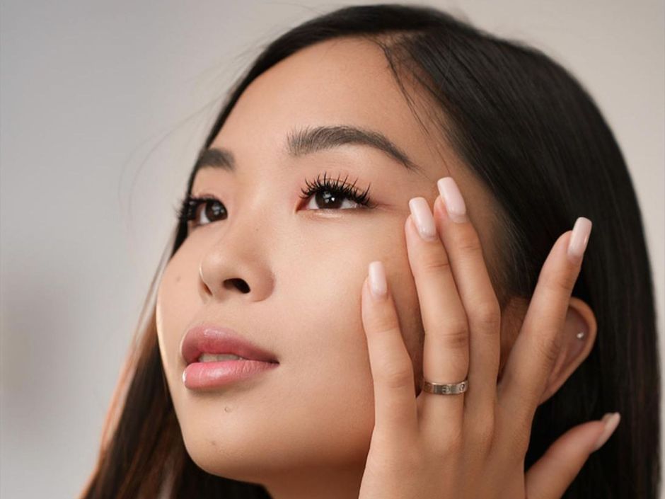 The woman is wearing a ring on her finger and touching her face.