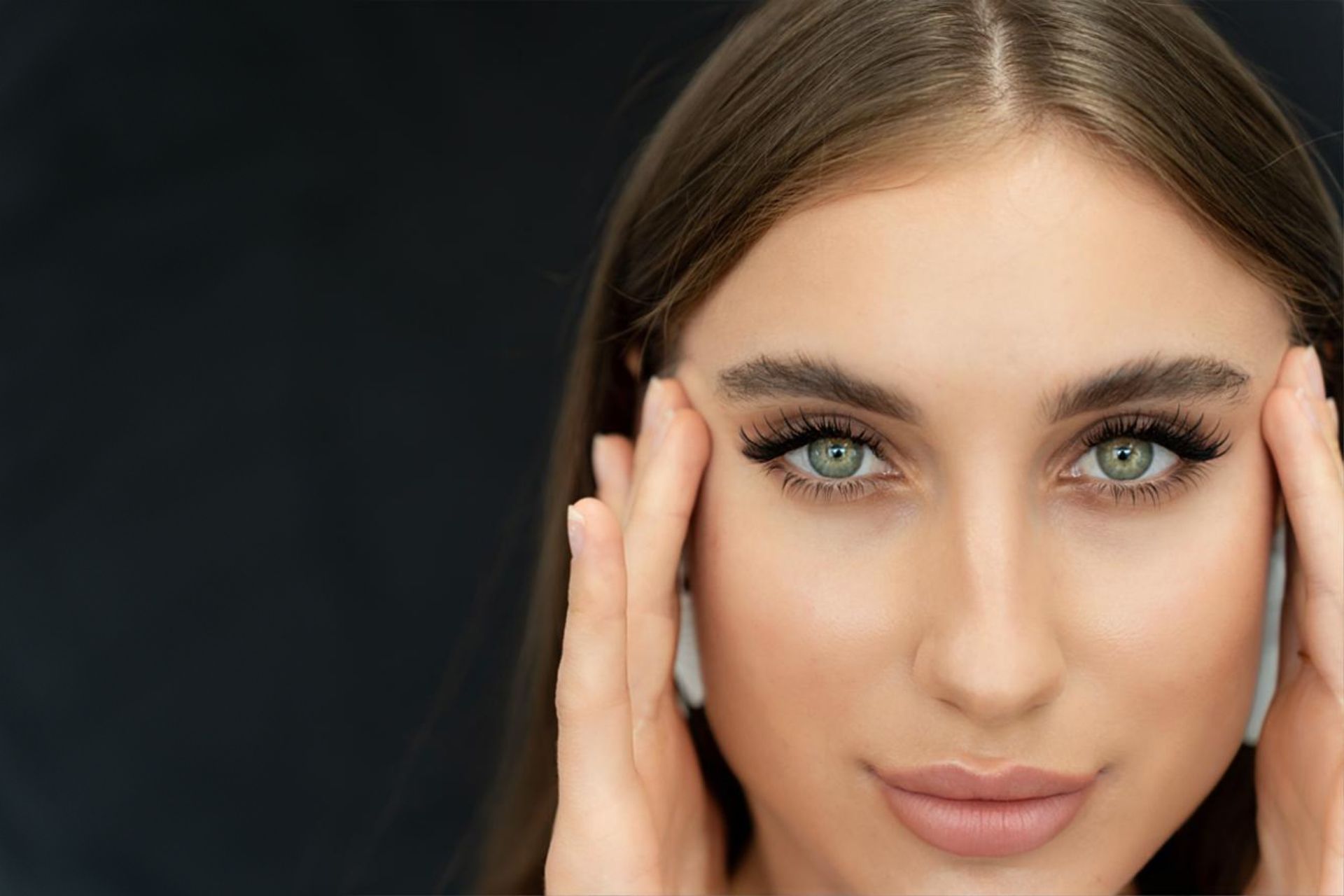 A close up of a woman 's face with her hands on her forehead.