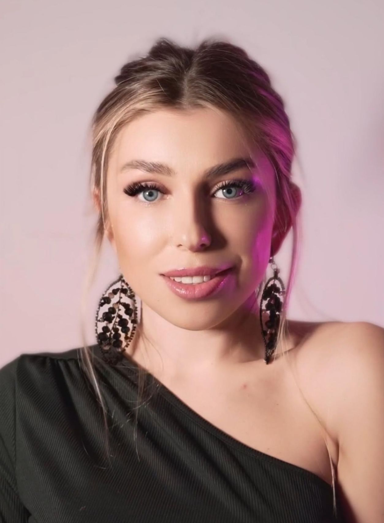 A woman wearing a black one shoulder top and earrings