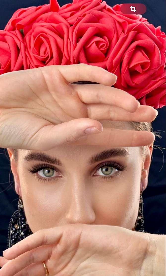 A woman is covering her face with her hands while wearing a crown of red roses.