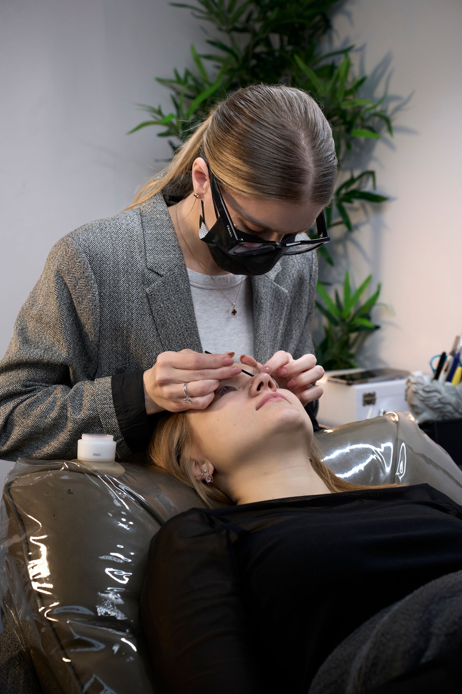 A woman is getting her eyelashes done in a salon while wearing a mask.