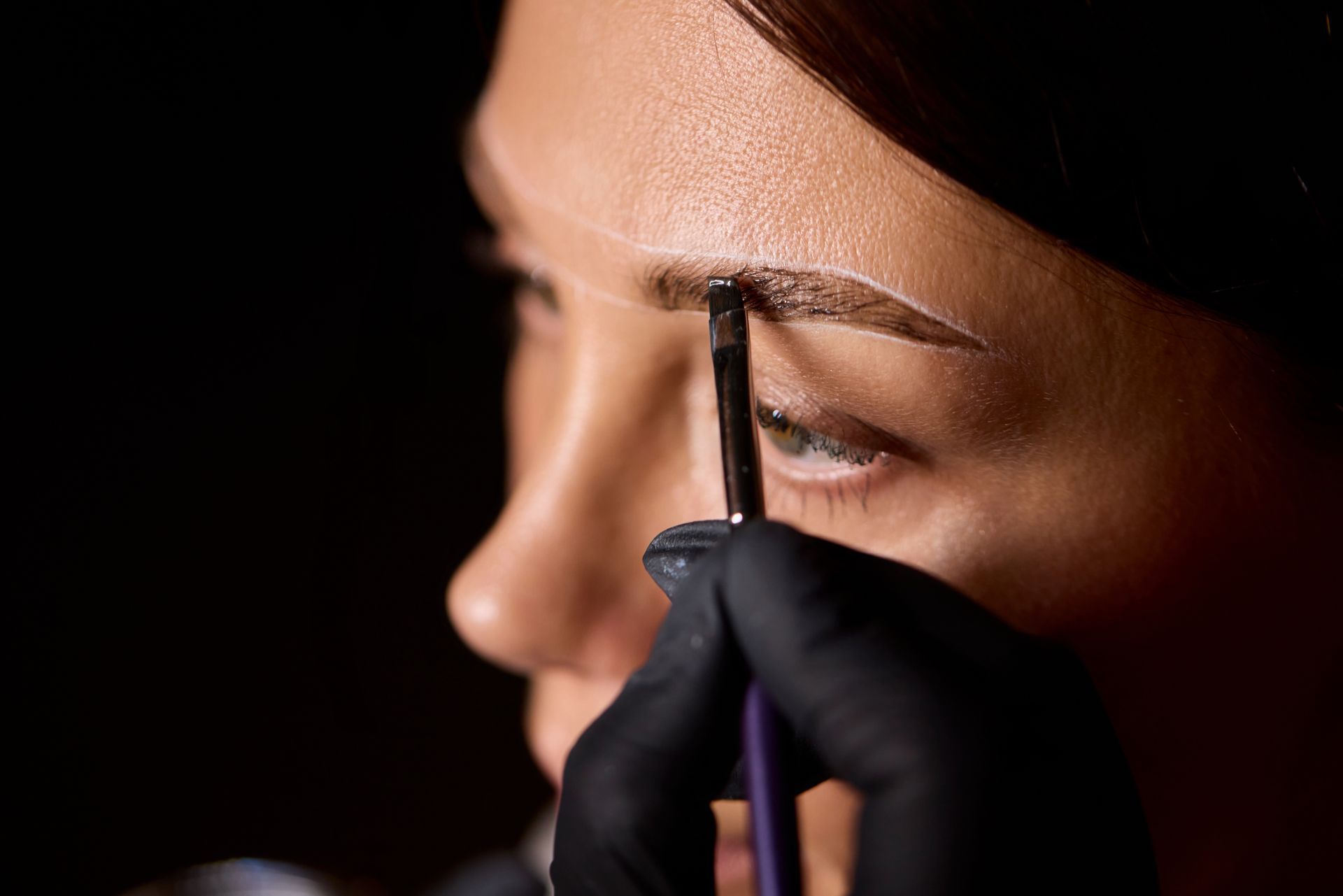 A woman is getting her eyebrows painted by a makeup artist.