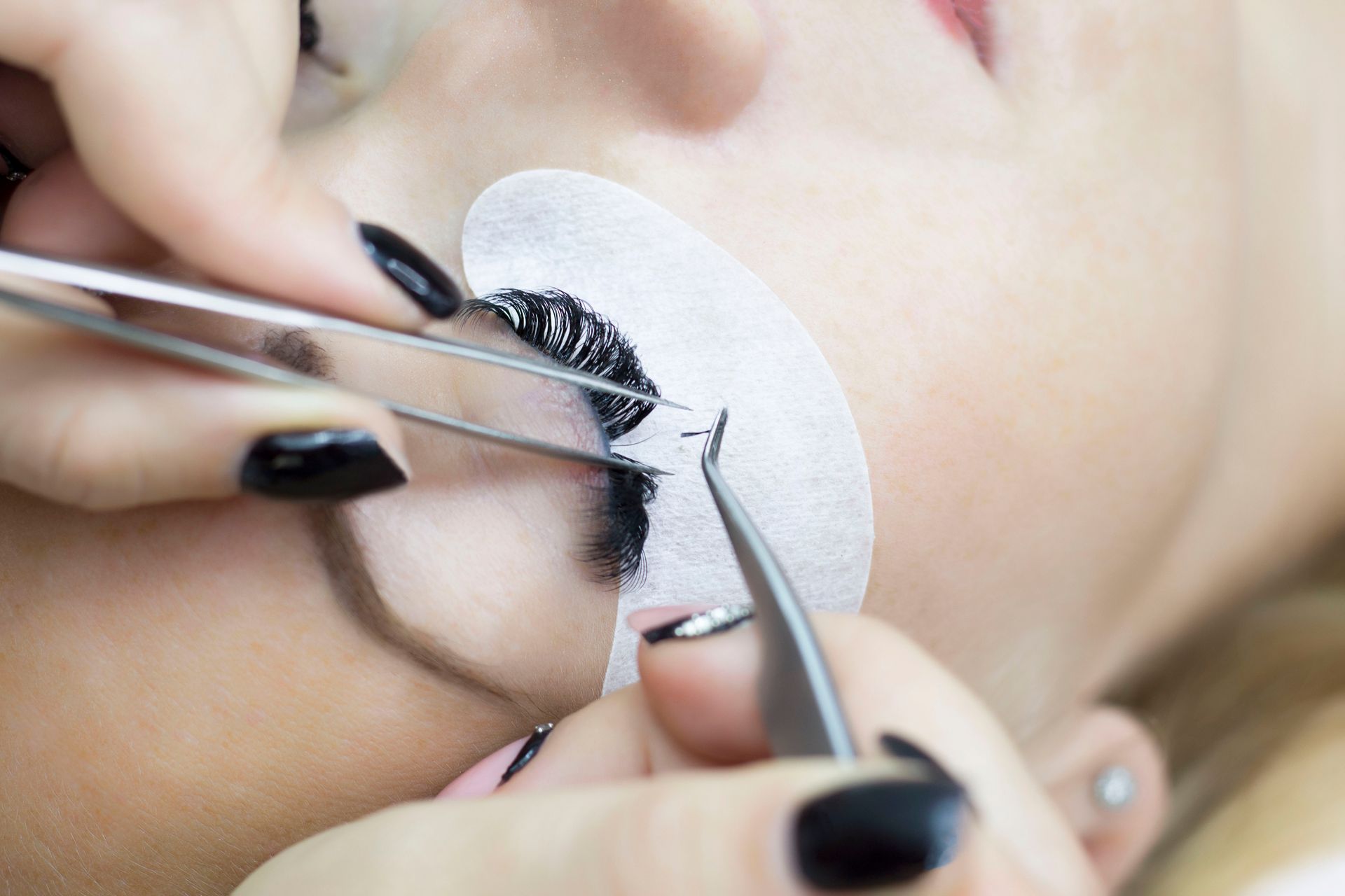 A woman with black nails is getting eyelash extensions.