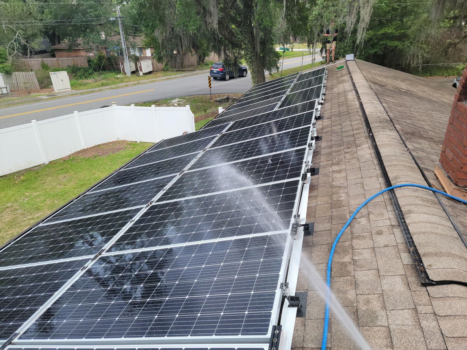 A person is cleaning solar panels on a roof with a hose.