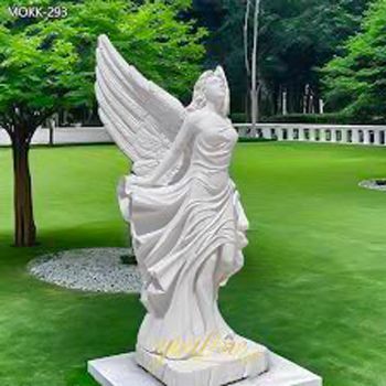 A statue of a woman with wings is standing in a park.
